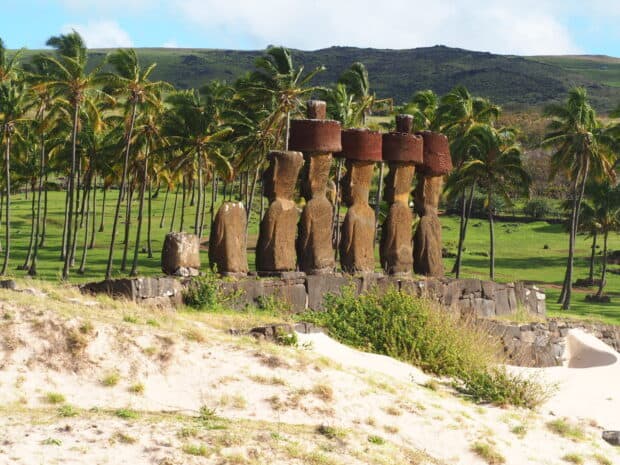 The Easter Island statues are standing in a vibrant green landscape with palm trees and hills, HD Desktop Wallpaper