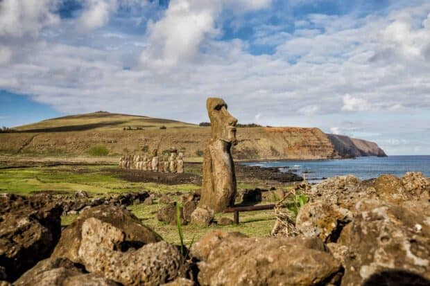 A large Easter Island statue stands near a row of smaller statues on a grassy coastline, HD Desktop Wallpaper