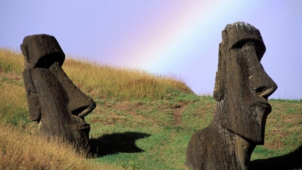 Two Easter Island statues stand on grassy hill under a rainbow in the sky, HD Desktop Wallpaper