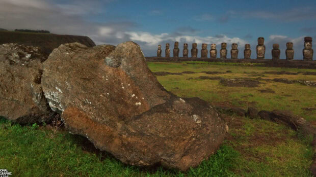 A large fallen stone statue lies on the grass with standing Easter Island statues in the background, HD Desktop Wallpaper