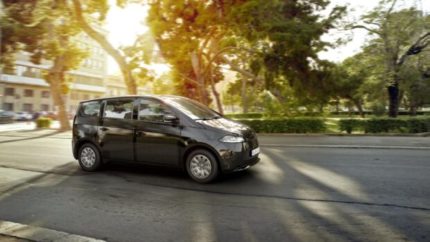 A black Sono Motors car is driving along a tree lined urban road in bright sunlight, 2K Desktop Wallpaper