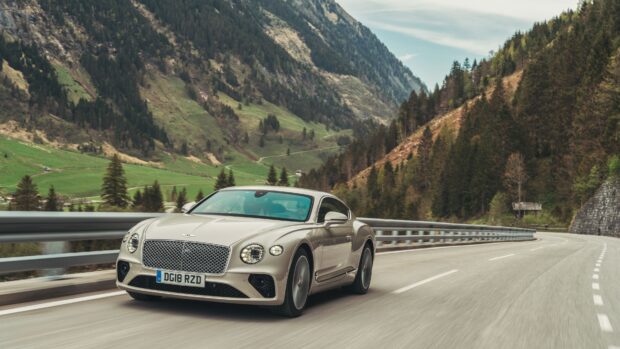 A Bentley Continental GT is driving on a winding road surrounded by green hills and trees, 4K Desktop Wallpaper