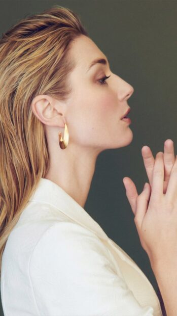 An elegant profile portrait of Elizabeth Debicki wearing gold earrings and a white jacket, 2K Phone Wallpaper