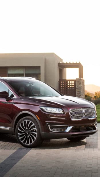 A maroon Lincoln car is parked outside a modern building during sunset in this Lincoln Car Wallpapers, 4K Phone Wallpaper