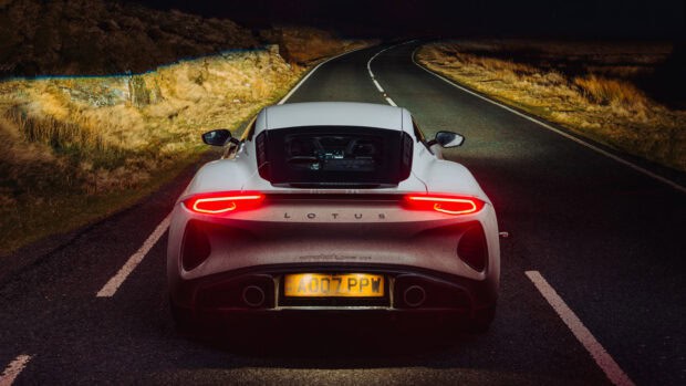 A Lotus Emira is shown from the rear on a dark winding road under night light, 2K Desktop Wallpaper