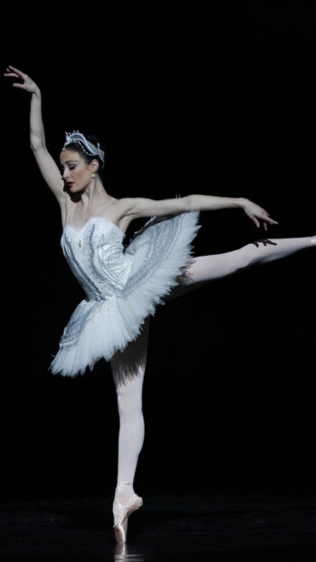 A ballet dancer performs an elegant pose with a white tutu on a dark stage, HD Phone Wallpaper