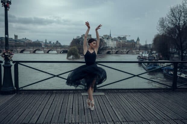 A ballet dancer in a black dress is gracefully posing on a wooden bridge by the river, HD Desktop Wallpaper