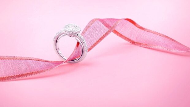A sparkling diamond ring is elegantly wrapped with a pink ribbon on a soft pink surface, HD Desktop Wallpaper