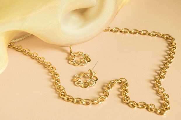 A gold chain necklace and matching earrings are displayed on a soft beige surface, HD Desktop Wallpaper