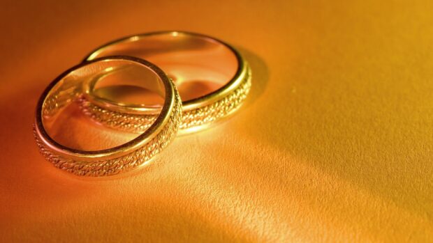 Two elegant gold wedding rings resting on an orange textured surface with detailed patterns, HD Desktop Wallpaper