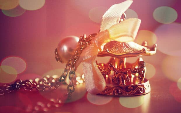 A delicate golden carousel pendant with a pearl and ribbon on a soft background, 2K Desktop Wallpaper