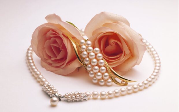A close up of pearl jewelry placed with two pink roses on a white surface featuring delicate details, 2K Desktop Wallpaper