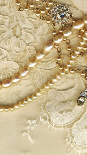 A close up view of a pearl necklace with a sparkling gemstone pendant on lace fabric, HD Mobile Wallpaper