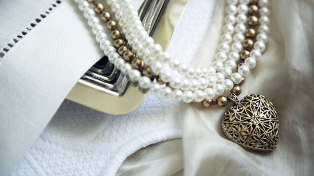 An elegant pearl necklace with a decorative heart pendant rests on soft white fabric, 4K Desktop Wallpaper