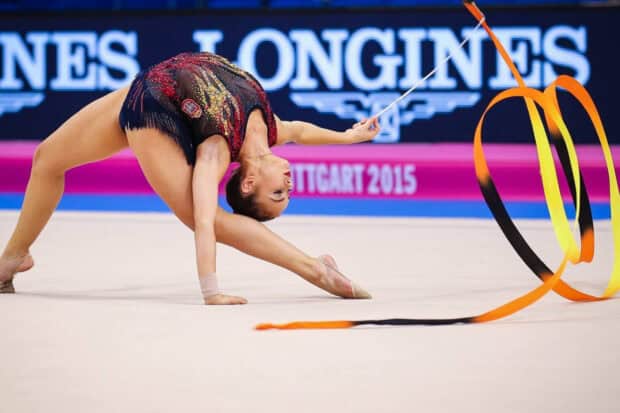 A rhythmic gymnastics athlete bends gracefully while performing with a ribbon during a competition, HD Desktop Wallpaper