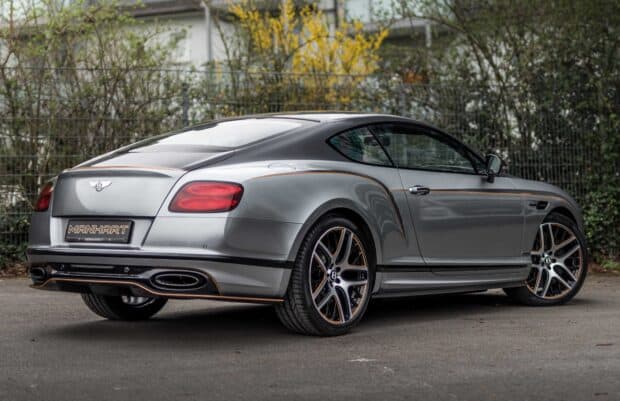 A silver Bentley Continental GT is parked near a fence with greenery in the background, HD Desktop Wallpaper
