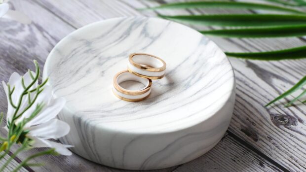 Two wedding rings rest on a round marble plate surrounded by white flowers and green leaves, 4K Desktop Wallpaper