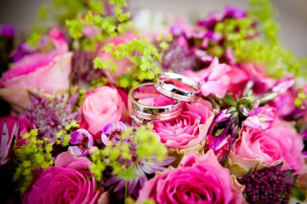Two shiny wedding rings are placed on a vibrant bouquet of pink roses and greenery, HD Desktop Wallpaper