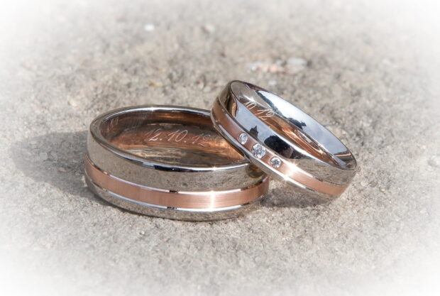Two wedding rings display diamonds and engraved dates on a sandy surface, HD Desktop Wallpaper