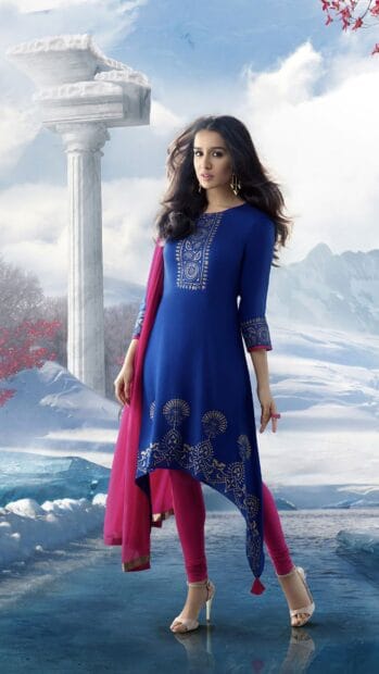 A Bollywood Wallpapers features a woman in a blue traditional outfit standing near a ancient column, 4K Phone Wallpaper