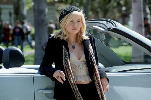 Elisha Cuthbert stands confidently beside a white convertible car wearing a black jacket and beanie, 2K Desktop Wallpaper