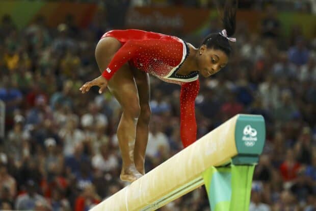 A gymnast concentrates intensely while performing on the balance beam during a competition, HD Desktop Wallpaper