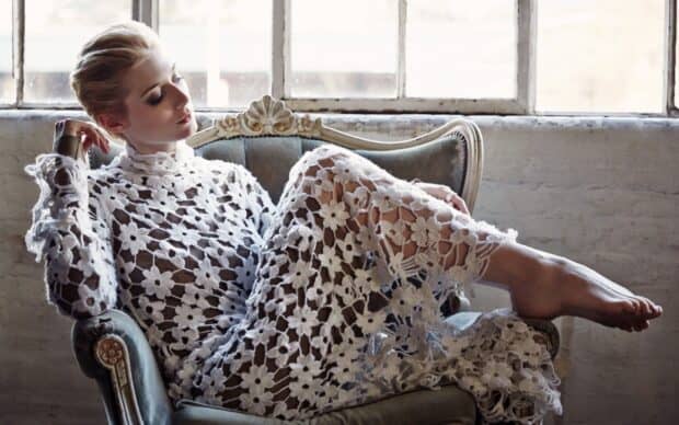 Elizabeth Debicki wears a white floral lace dress while sitting on a vintage chair near a large window, HD Desktop Wallpaper