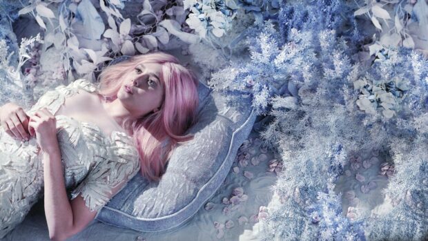 Elizabeth Olsen lies surrounded by blue and pink flowers with a thoughtful expression, 2K Desktop Wallpaper