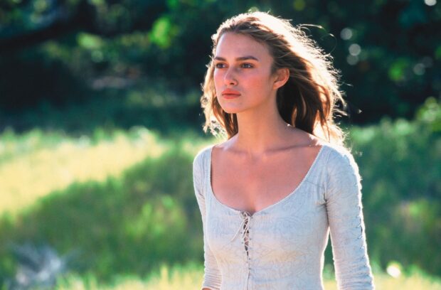 Elizabeth Swann from Pirates Of The Caribbean stands in a sunlit field with greenery behind her, HD Desktop Wallpaper