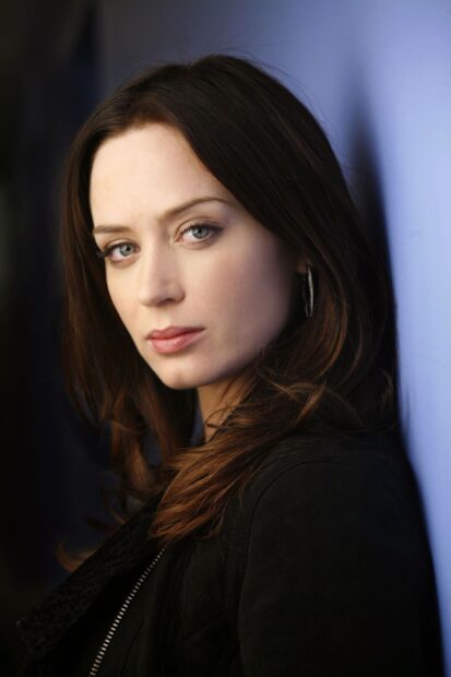 Emily Blunt looks thoughtfully at the camera standing near a blue wall, HD Mobile Wallpaper