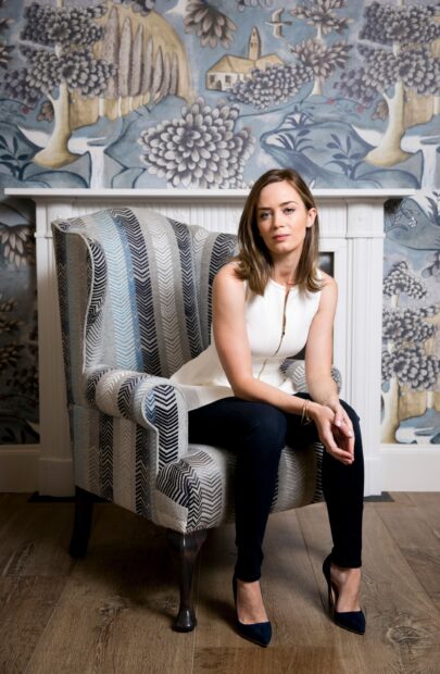 Emily Blunt sitting thoughtfully in a patterned armchair with a floral wallpaper background, 2K Mobile Wallpaper