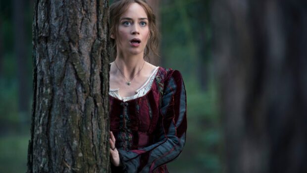 Emily Blunt shows a shocked expression while standing behind a tree in the forest, 2K Desktop Wallpaper