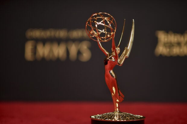 A golden Emmy Awards statuette is displayed on a red surface with a blurred background, HD Desktop Wallpaper