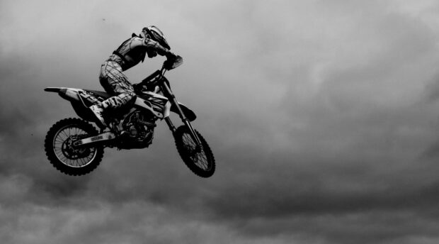 A rider on an enduro motorbike is performing a jump against a cloudy sky, 4K Desktop Wallpaper