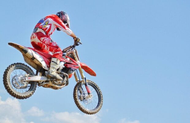 A rider performing a high jump on an enduro motorbike under a clear blue sky, 2K Desktop Wallpaper