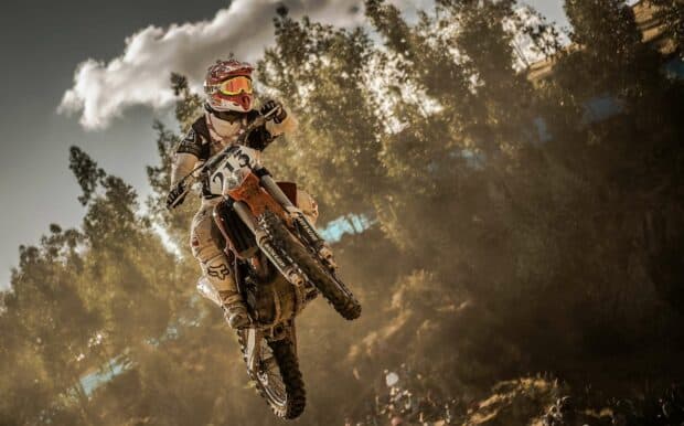A rider on an enduro motorbike jumps high through a dusty forest trail, HD Desktop Wallpaper