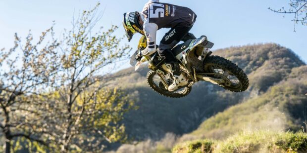 A rider on an enduro motorbike is performing a jump outdoors in the mountains, 2K Desktop Wallpaper