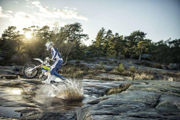 A rider on an enduro motorbike jumps over a water splash on rocky terrain, HD Desktop Wallpaper