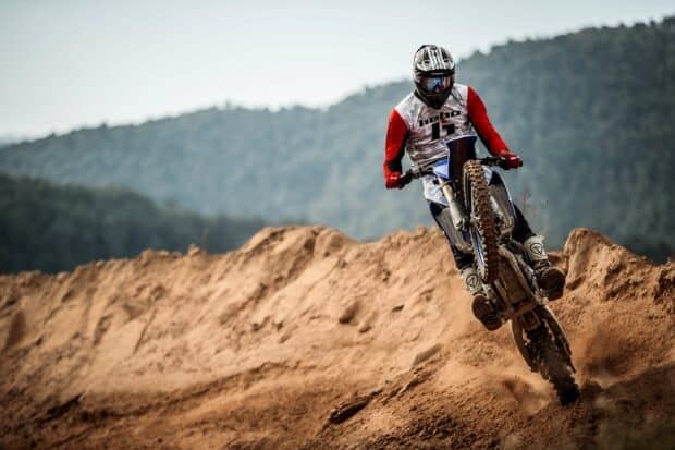 A rider on an enduro motorbike doing a wheelie on a dirt track with hills in the background, 2K Desktop Wallpaper
