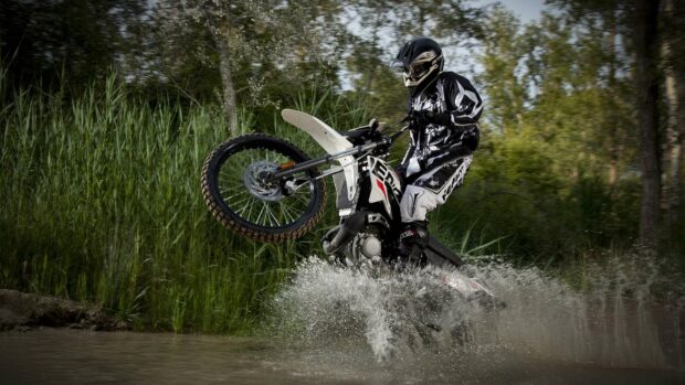 A rider on an enduro motorbike splashes through water while lifting the front wheel, 4K Desktop Wallpaper