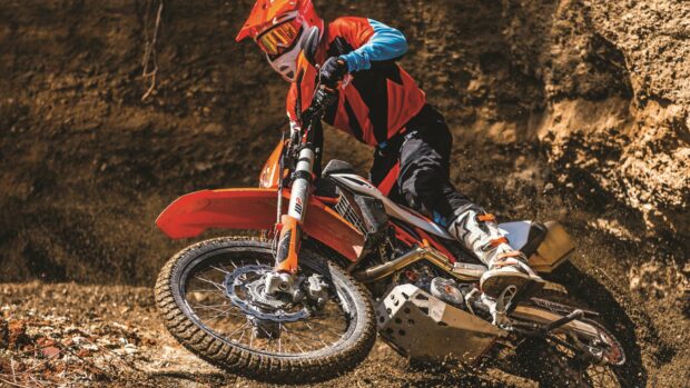 A rider on an enduro motorbike is speeding through rough terrain while kicking up dirt, 4K Desktop Wallpaper