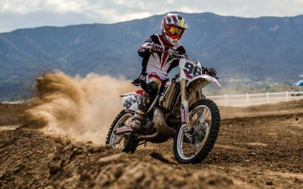 A rider performs an intense turn on an enduro motorbike kicking up dust on the dirt track, 2K Desktop Wallpaper