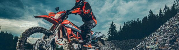 A rider on an orange enduro motorbike navigating rocky terrain under a cloudy sky, 4K Desktop Wallpaper