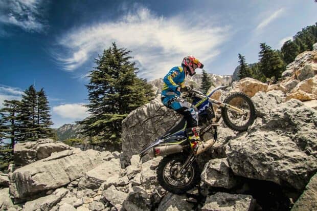 A rider on an enduro motorbike climbs rocky mountain terrain under a cloudy sky, HD Desktop Wallpaper