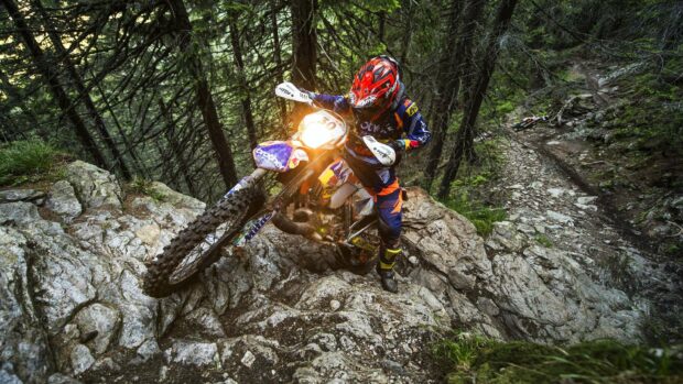 A rider on an enduro motorbike climbs a rocky path through a dense forest, 2K Desktop Wallpaper