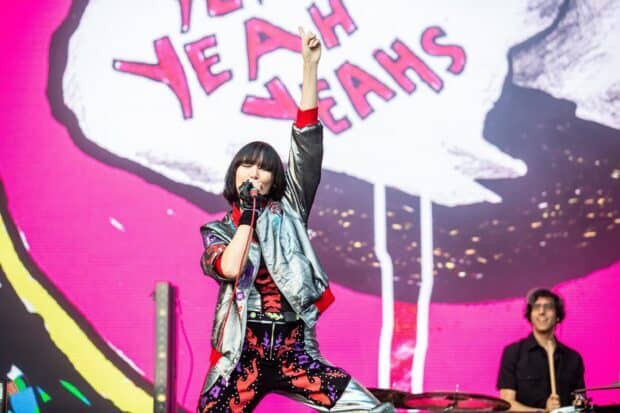 The lead singer of Yeah Yeah Yeahs is passionately performing on stage with vibrant visuals behind, 2K Desktop Wallpaper