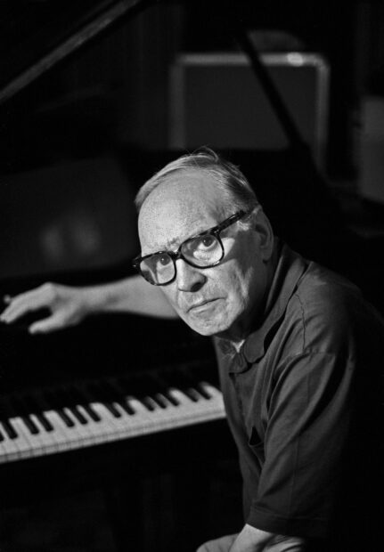 Ennio Morricone is sitting by a piano in this black and white portrait, HD Mobile Wallpaper