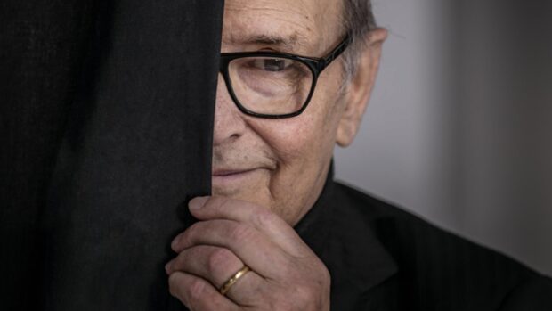 An elderly man wearing glasses holds black fabric close to his face in a thoughtful pose, 4K Desktop Wallpaper