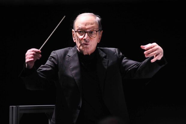 Ennio Morricone is leading an orchestra with expressive gestures during a live performance, 2K Desktop Wallpaper