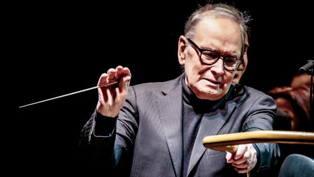 Ennio Morricone is seen conducting with passion in a dark setting, 2K Desktop Wallpaper